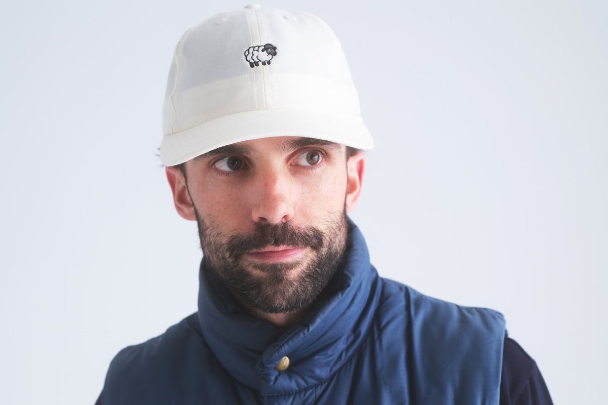 A man in a white Whim sheep cap and a navy quilted vest
