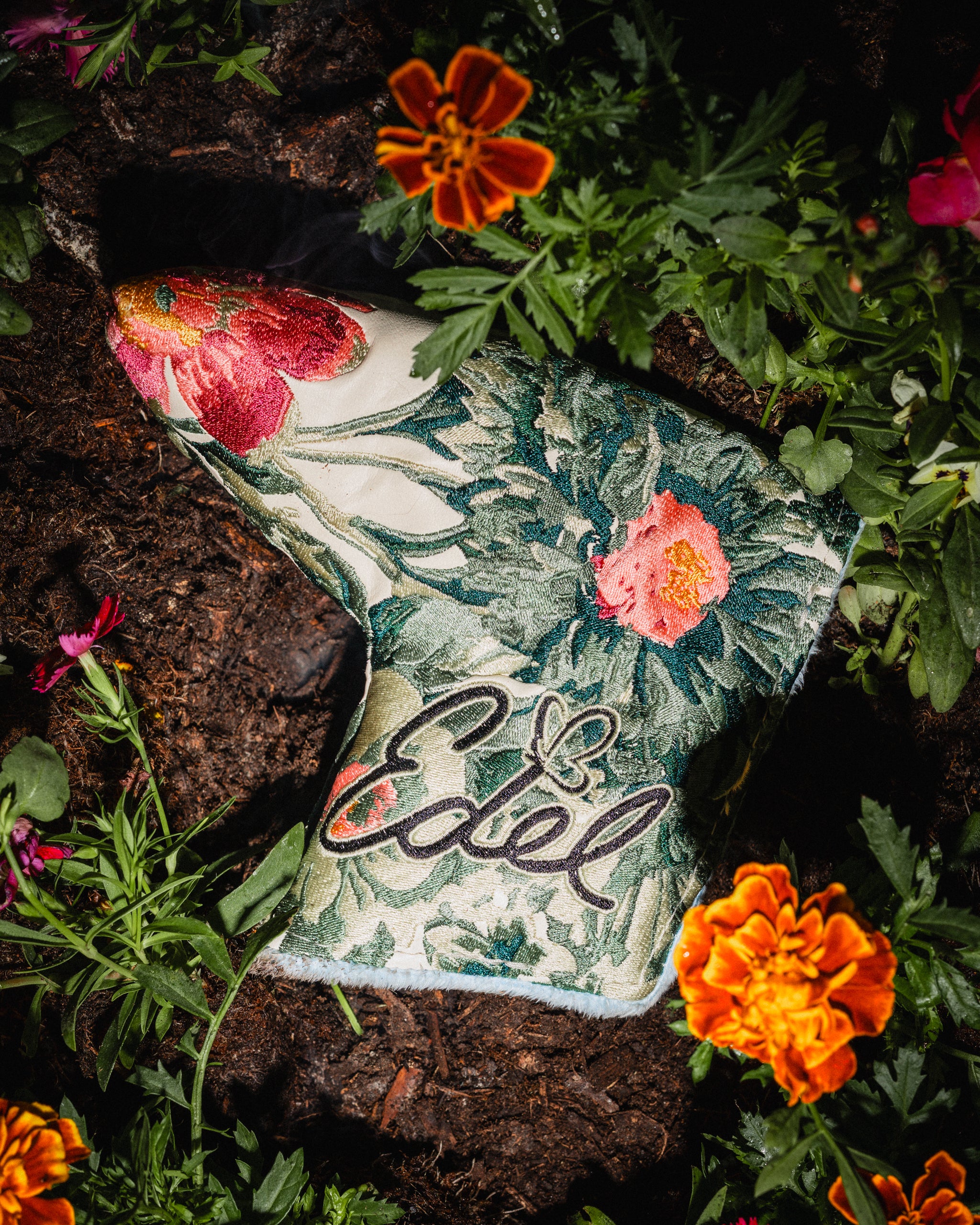 The Bloom headcover, floral print, on dark soil and marigolds