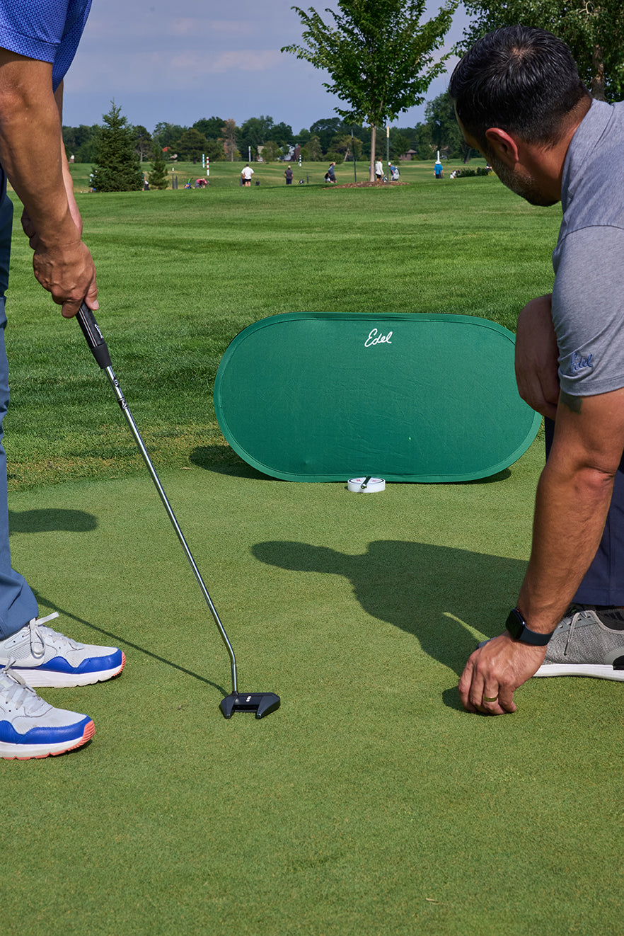 Two golfers running Edel&rsquo;s aim test on a practice green, one crouching to check the ball&rsquo;s line