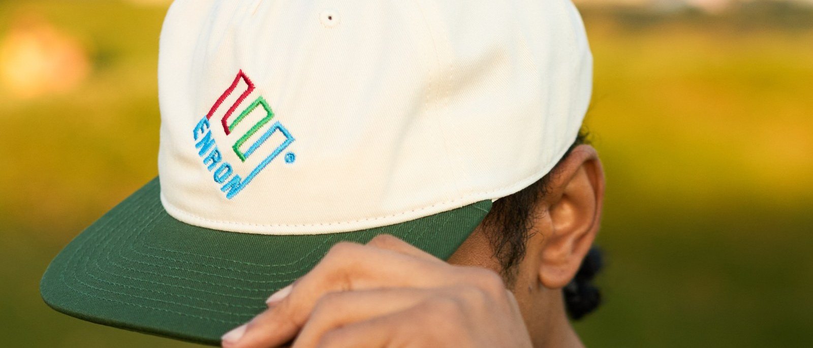 A golfer adjusting a cream and green Enron Pro E1 cap with the tilted E logo