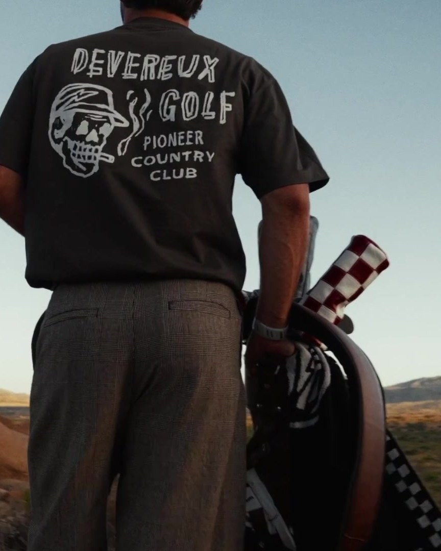 Two golfers from behind in the desert, one in a Devereux Pioneer Country Club tee