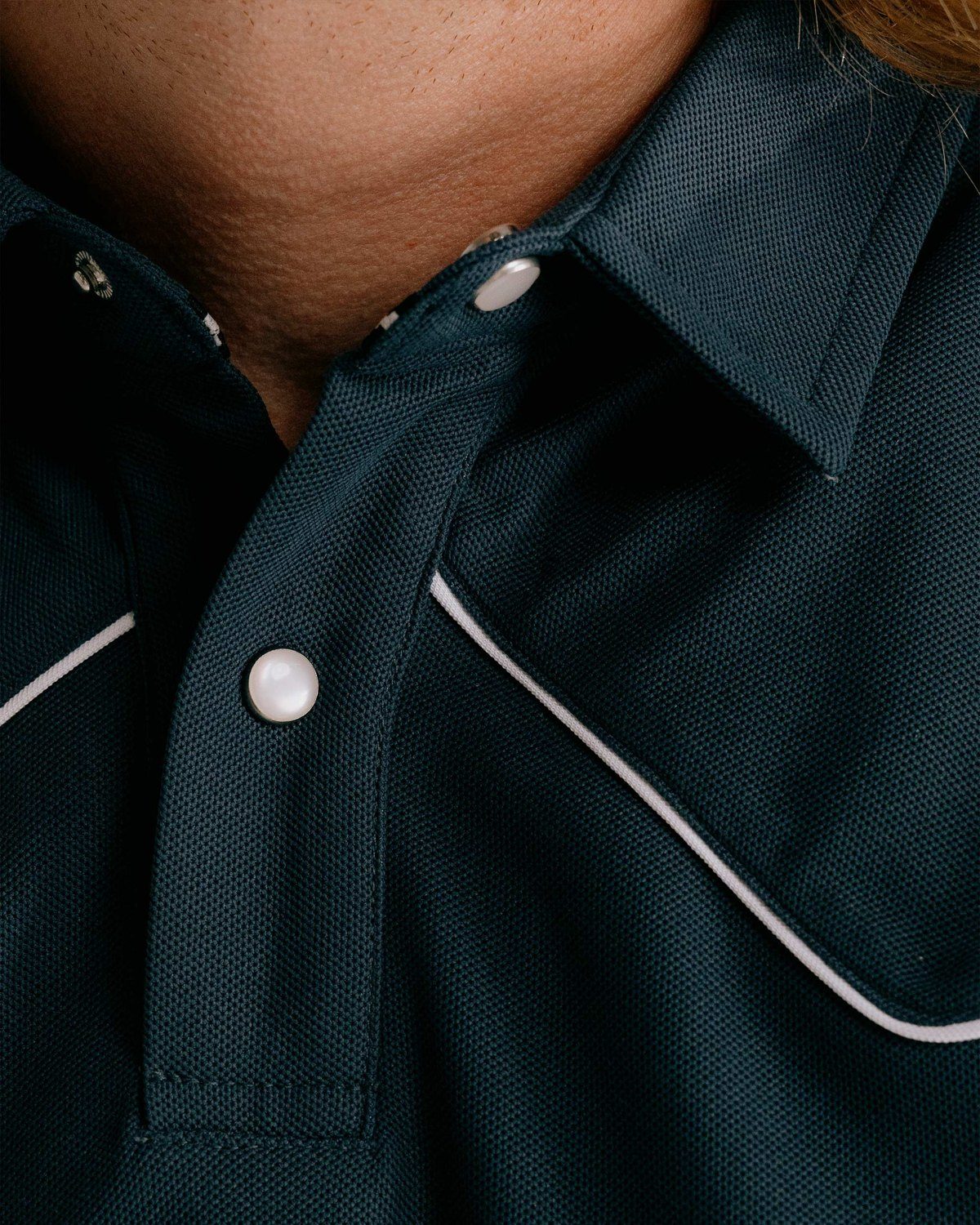 Close detail of a navy Devereux Western polo with white piping at the yoke