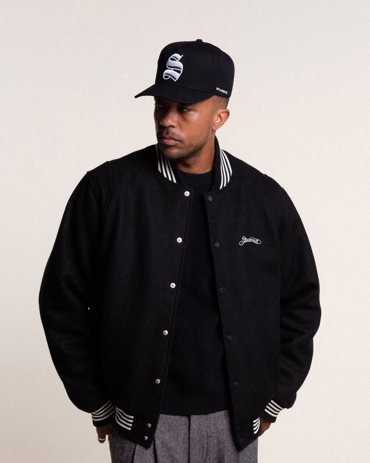 A man in a black Students Denali wool stadium jacket and an S cap