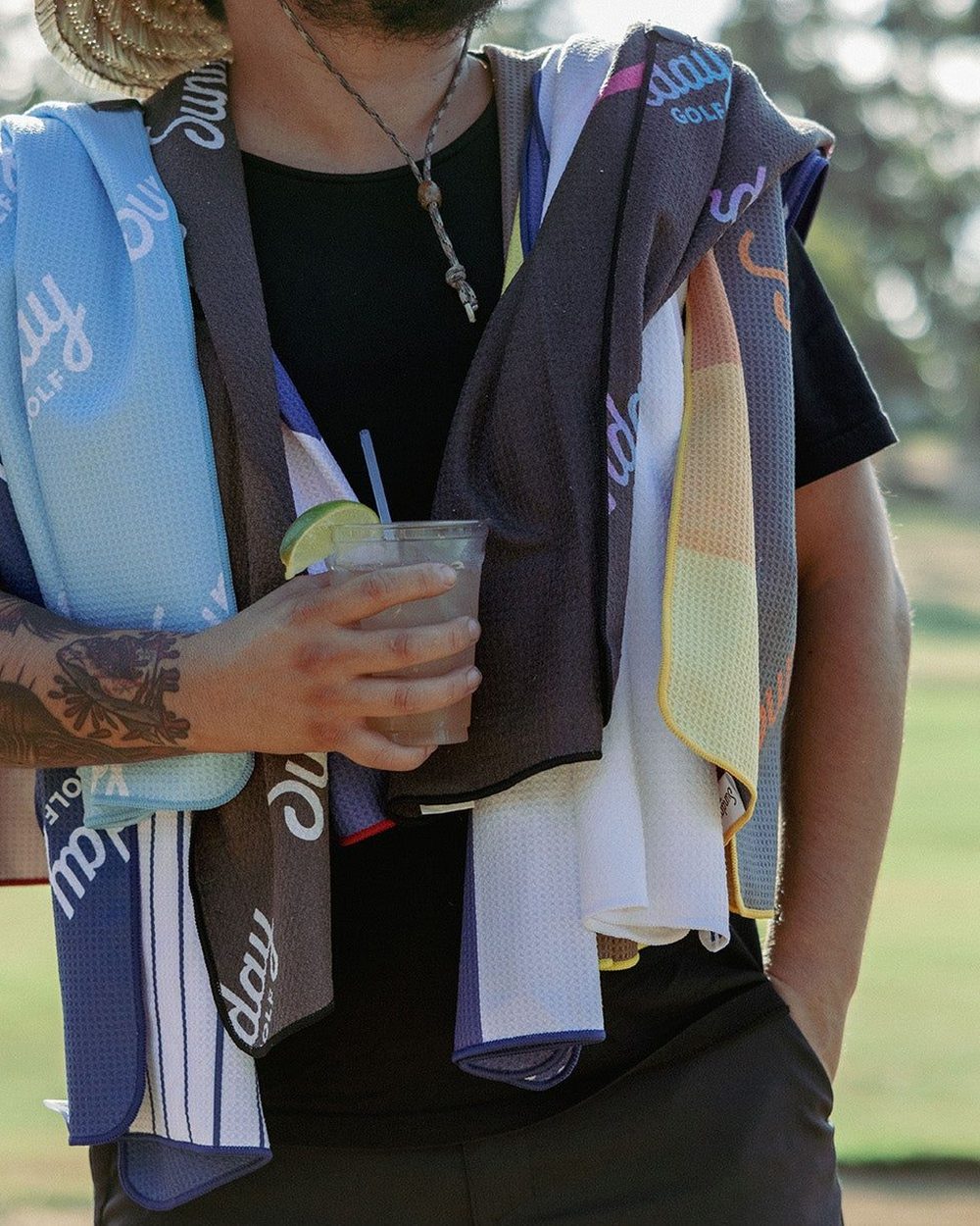 A golfer with a stack of Sunday Golf towels over his shoulders and a drink in his hand