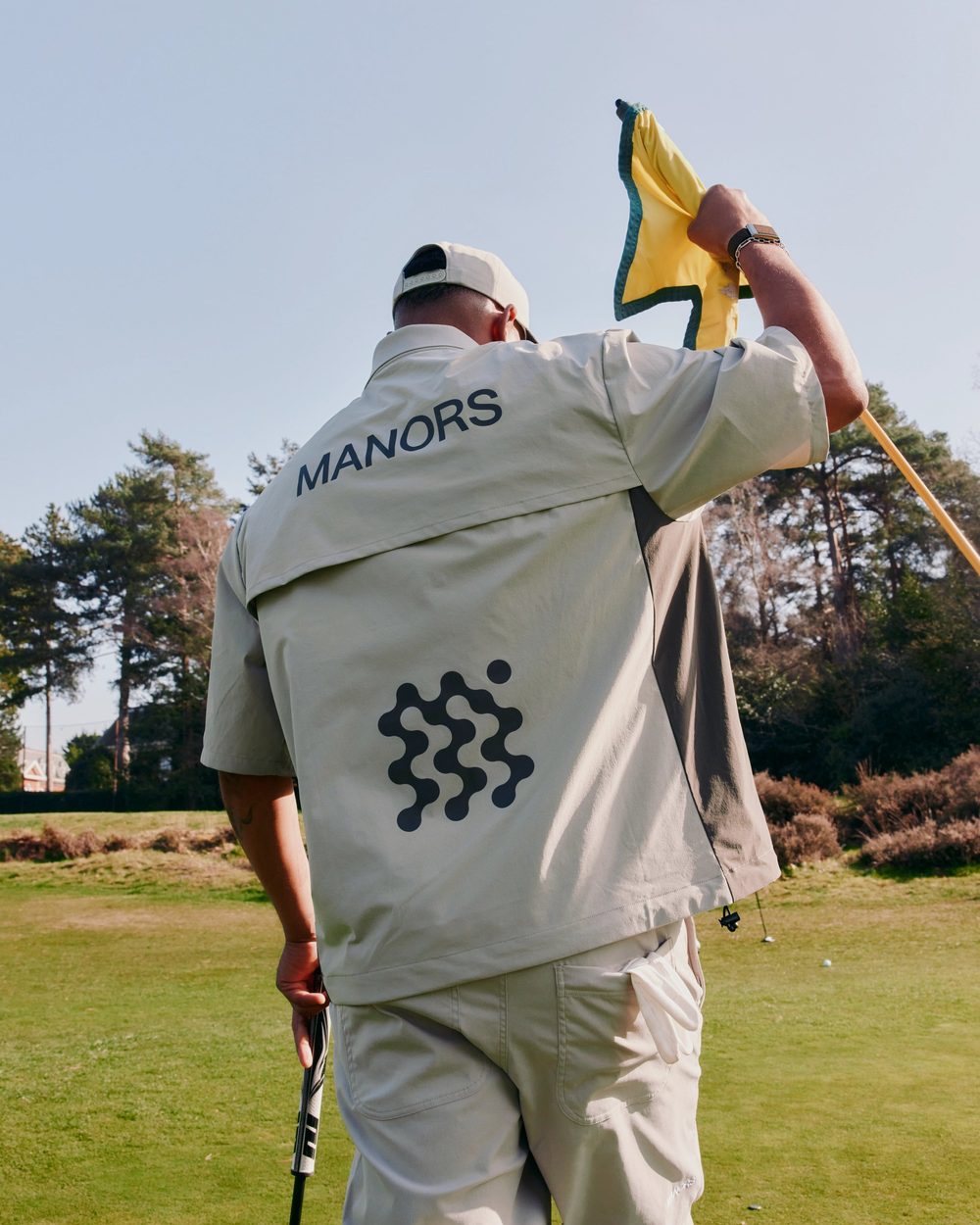 A golfer in a Manors jacket holding the pin with a yellow flag