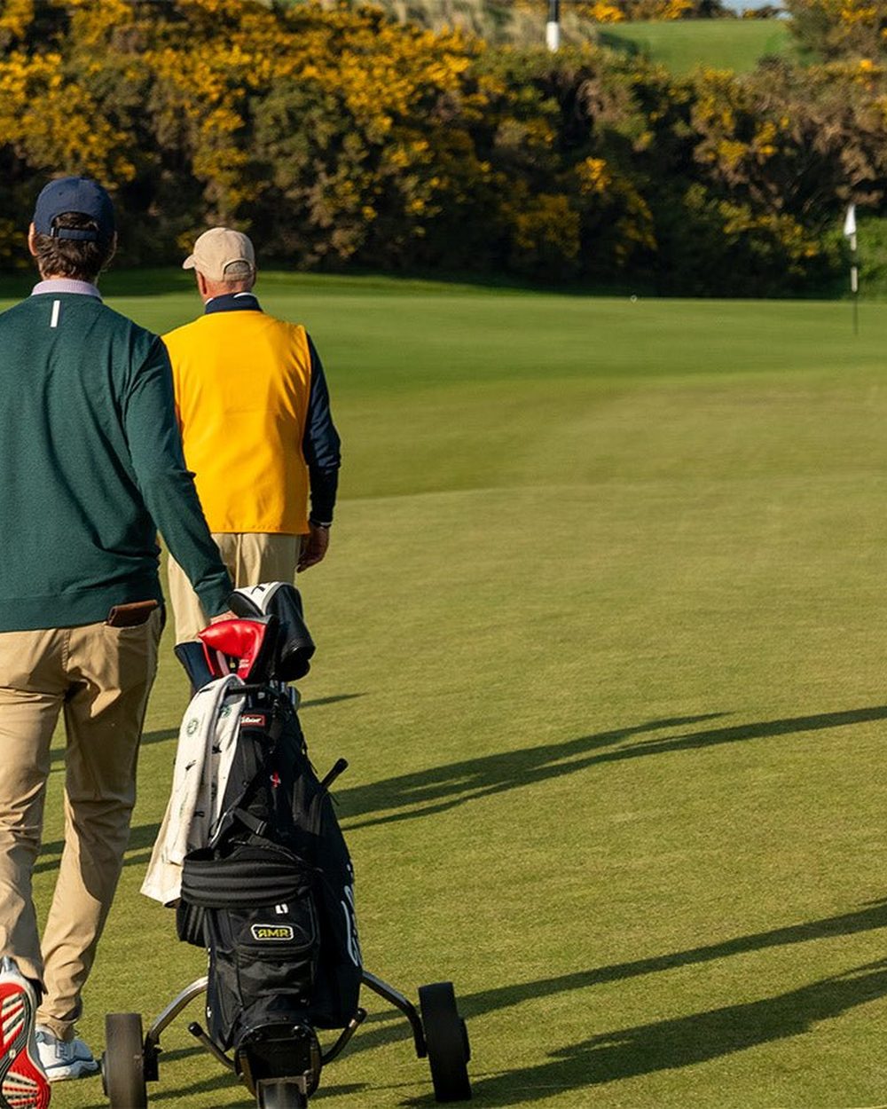 Two golfers walking down the fairway pushing their bags