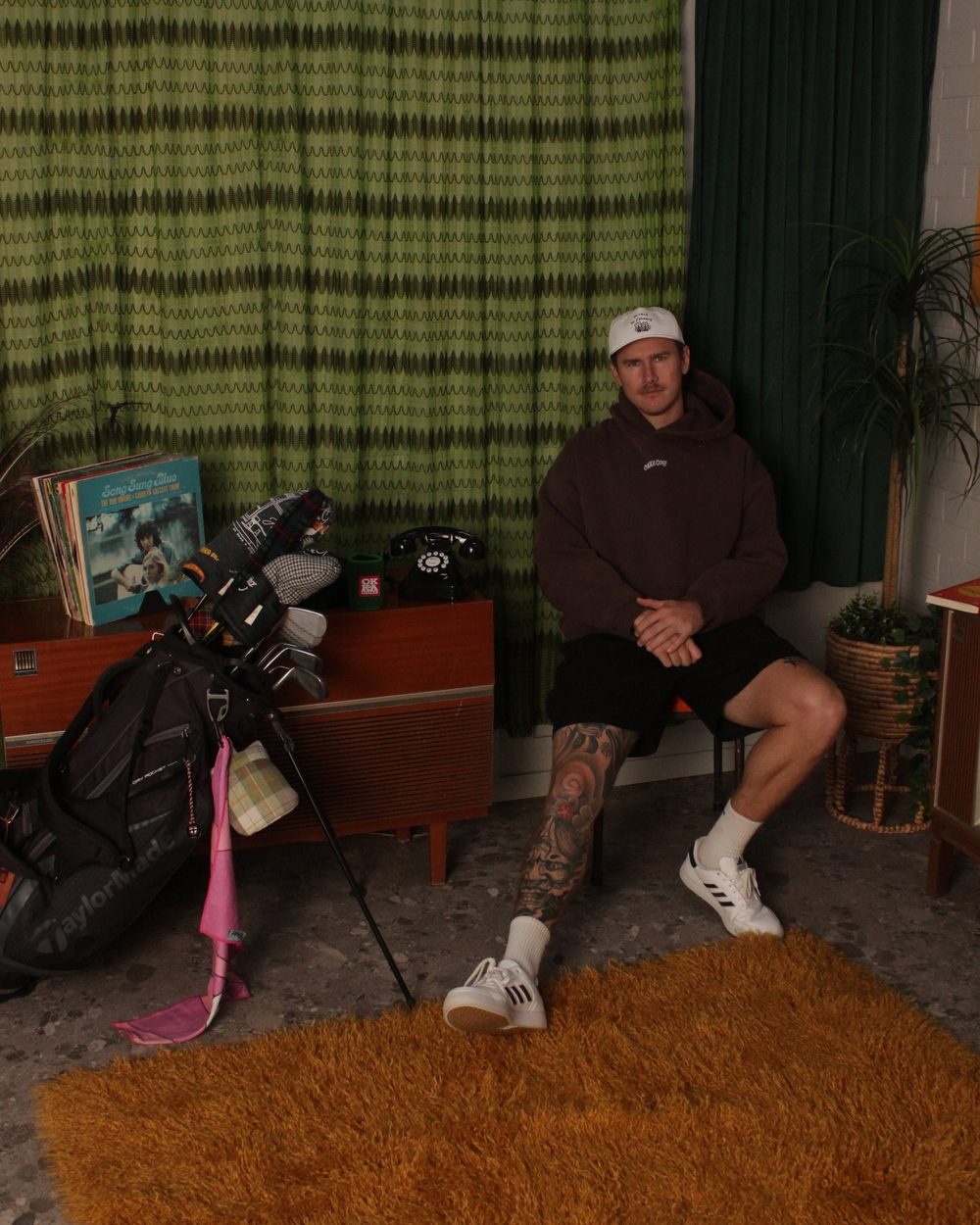 A man sitting in a room with a green plaid curtain and a golf bag beside him