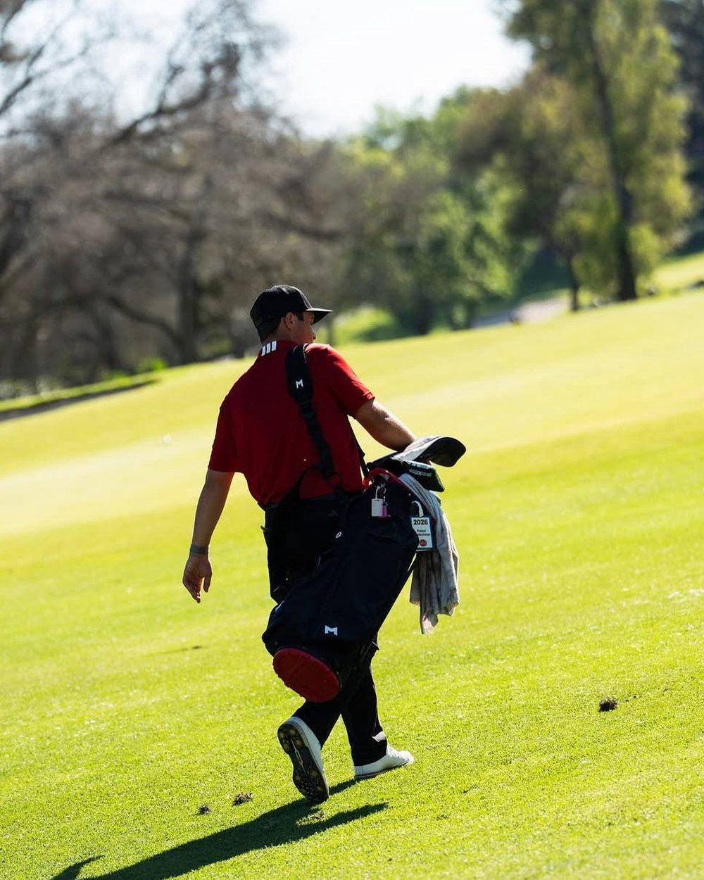 A golfer in a red shirt walking up the fairway carrying his bag