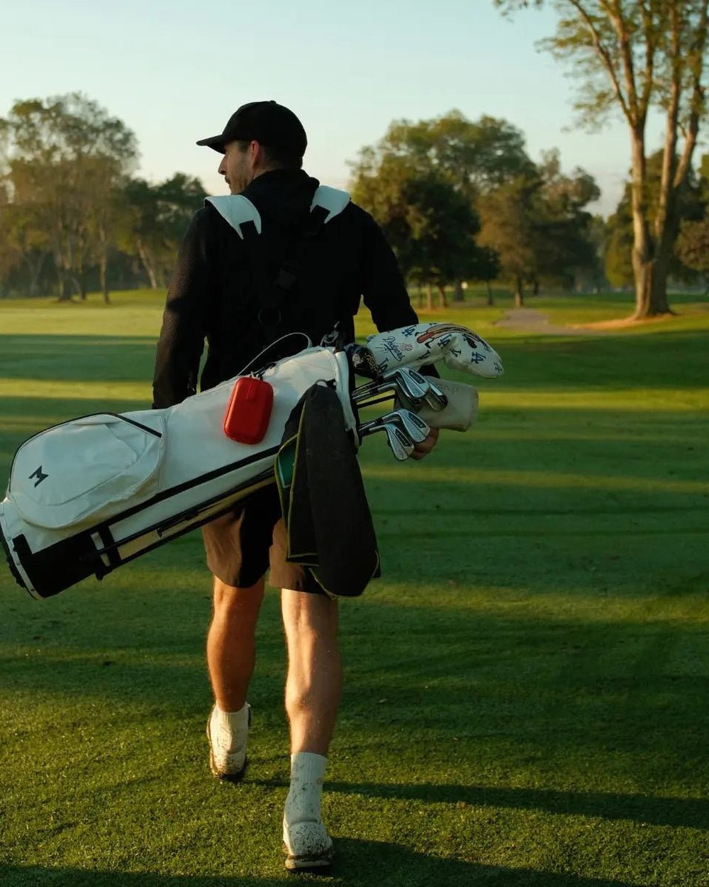 A golfer carrying a white stand bag toward the trees