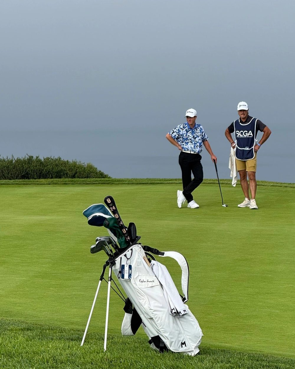 Two golfers on a green beside a white stand bag