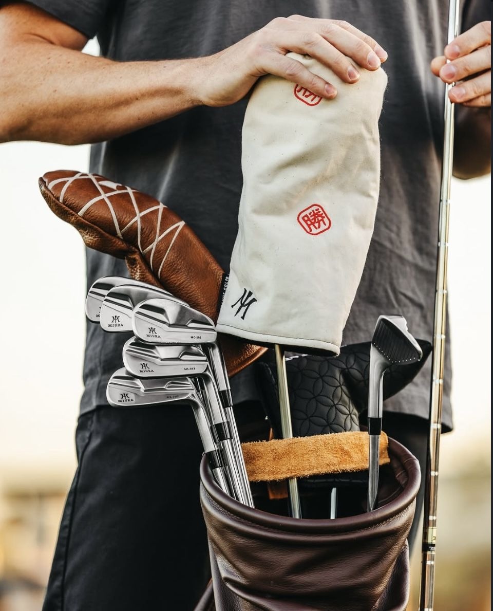 Tweed and stitched leather headcovers beside forged irons in a canvas carry bag