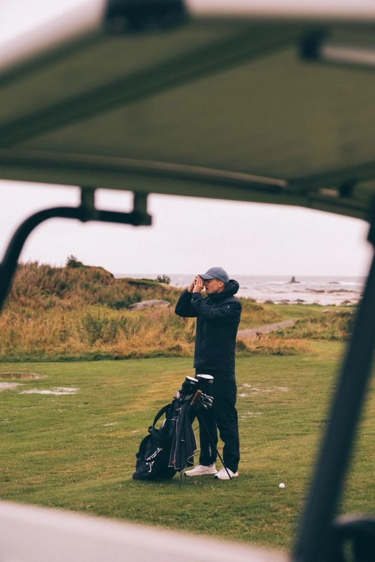 Golfer using rangefinder on coastal course seen through golf cart frame in moody light