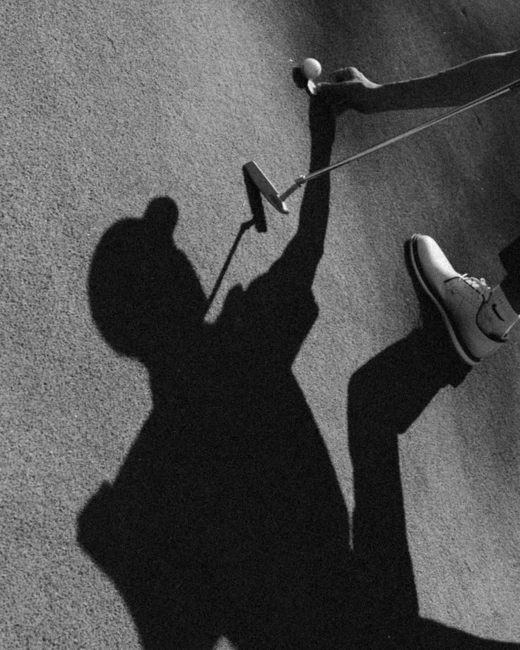 Black and white overhead shot of golfer shadow with putter and ball on green