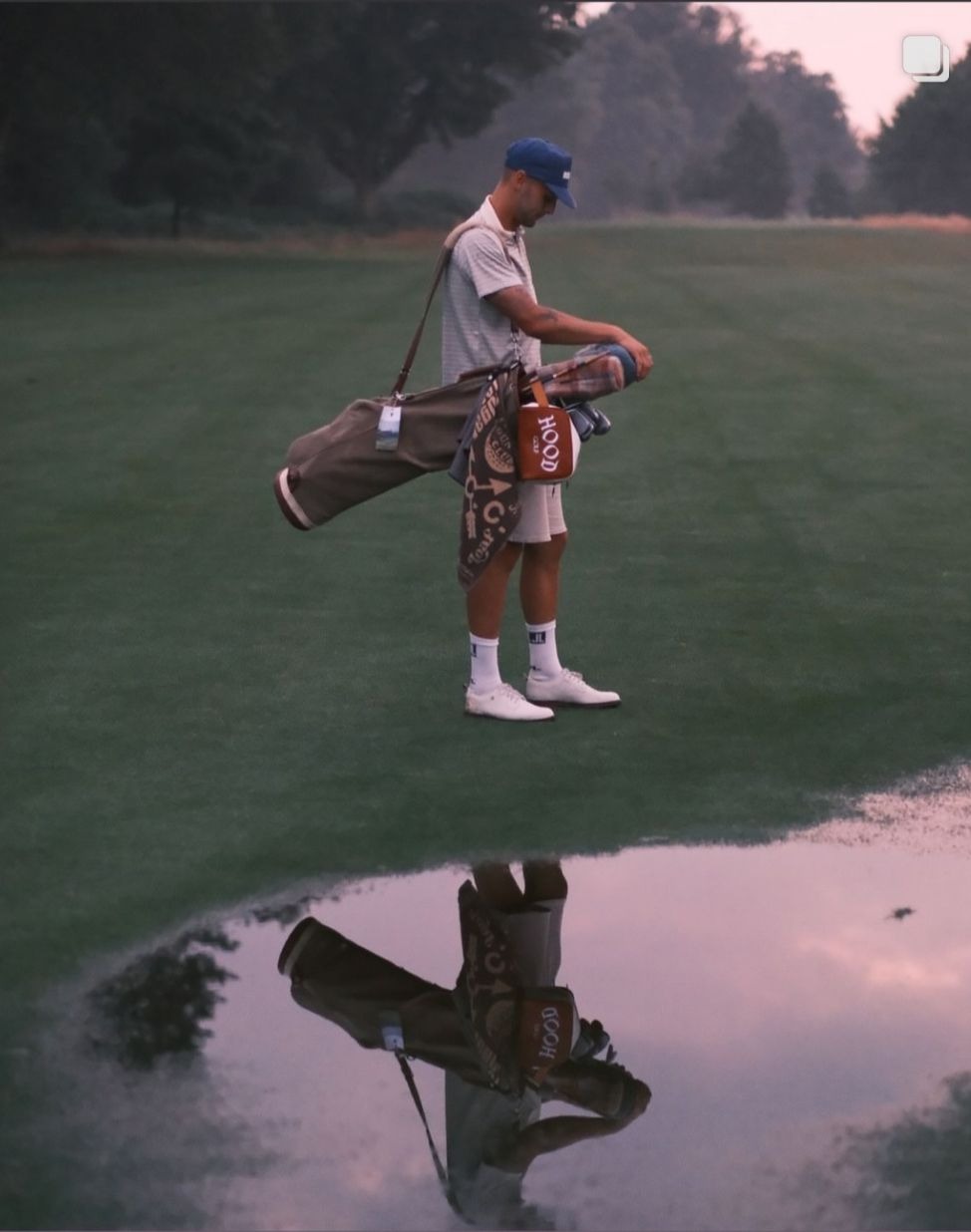 Walker with a carry bag reflected in still water on a course at first light
