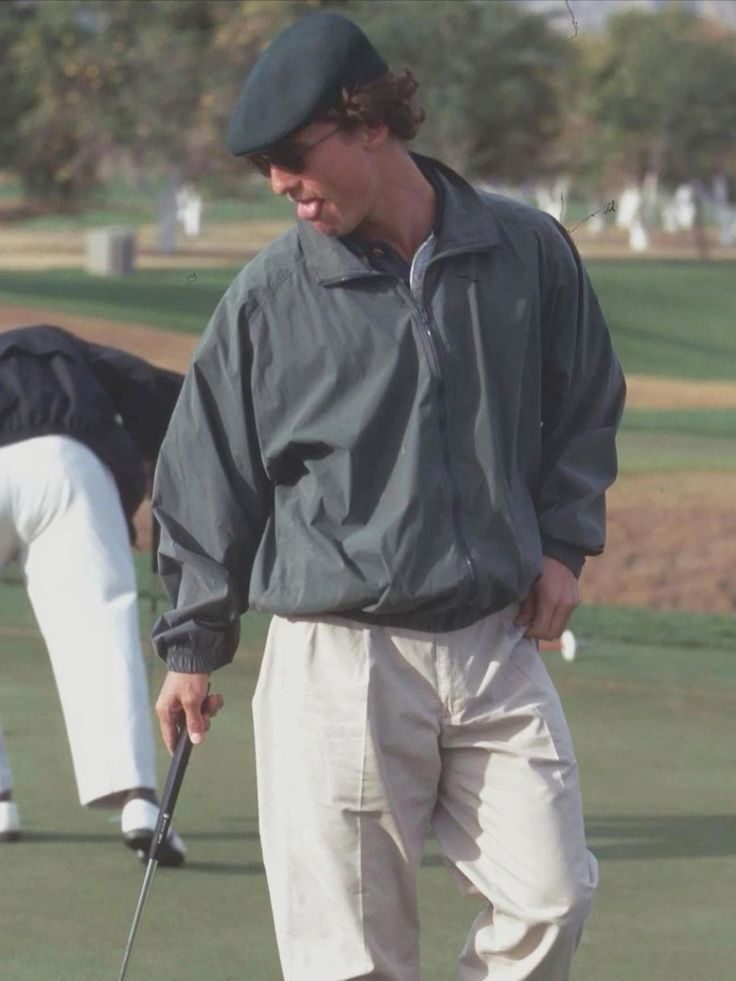 Golfer in grey windbreaker and flat cap with club on green in retro film style