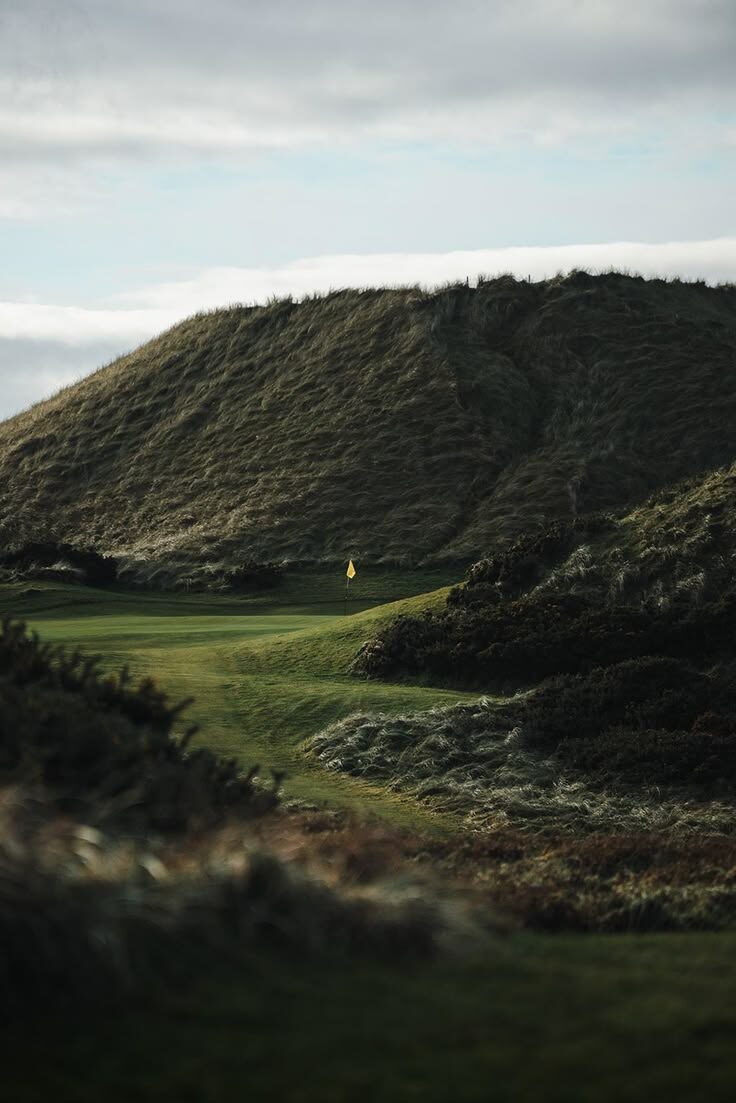 Dramatic links course with rugged hills and yellow flag under moody clouds