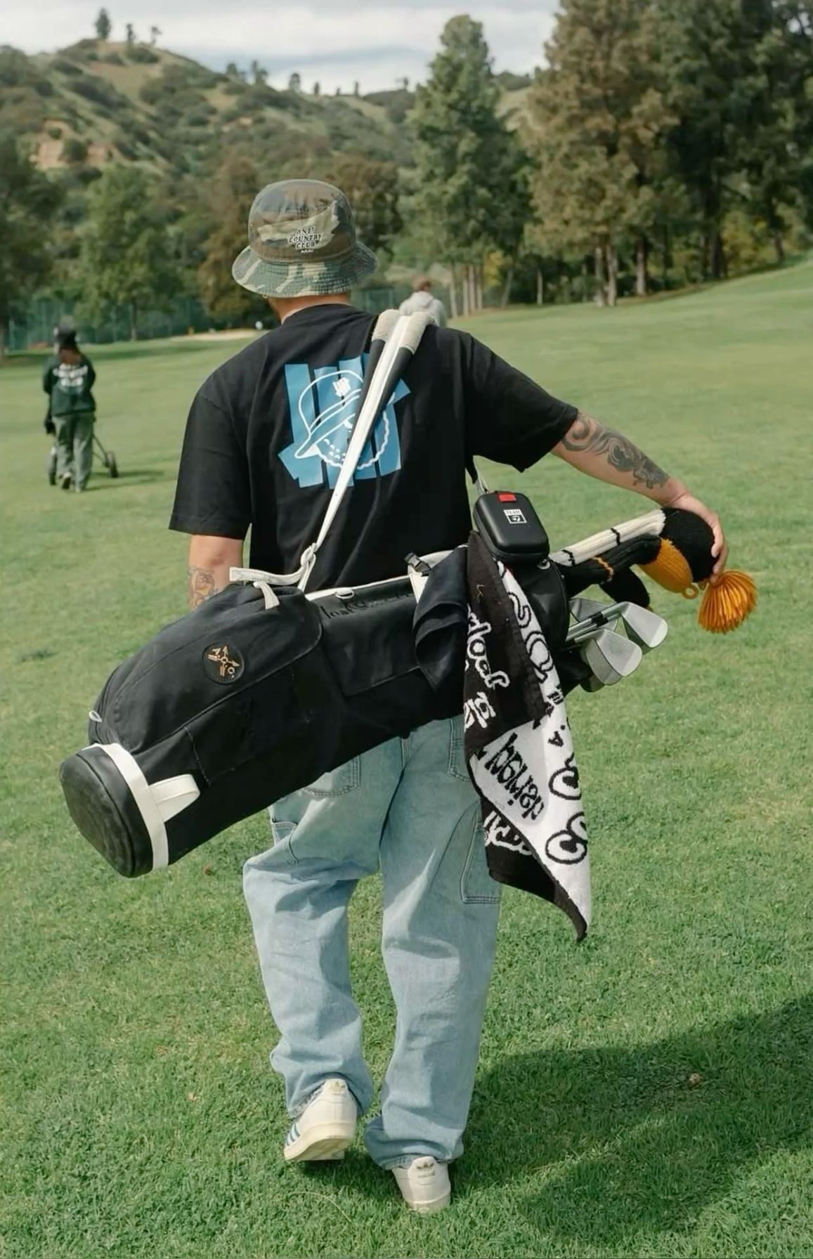 Golfer seen from behind carrying a black stand bag with a printed towel hanging off it