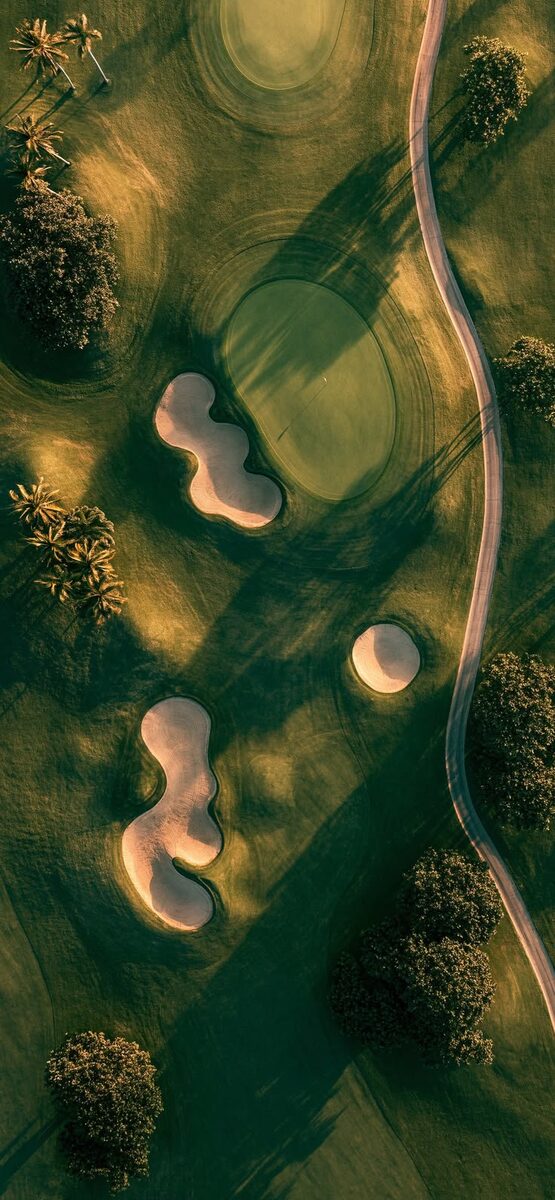 Aerial view of golf course with winding cart path and shaped bunkers at golden hour