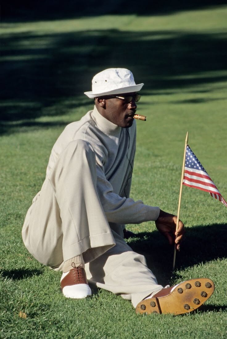 Golfer kneeling on course with cigar and small American flag in vintage bucket hat