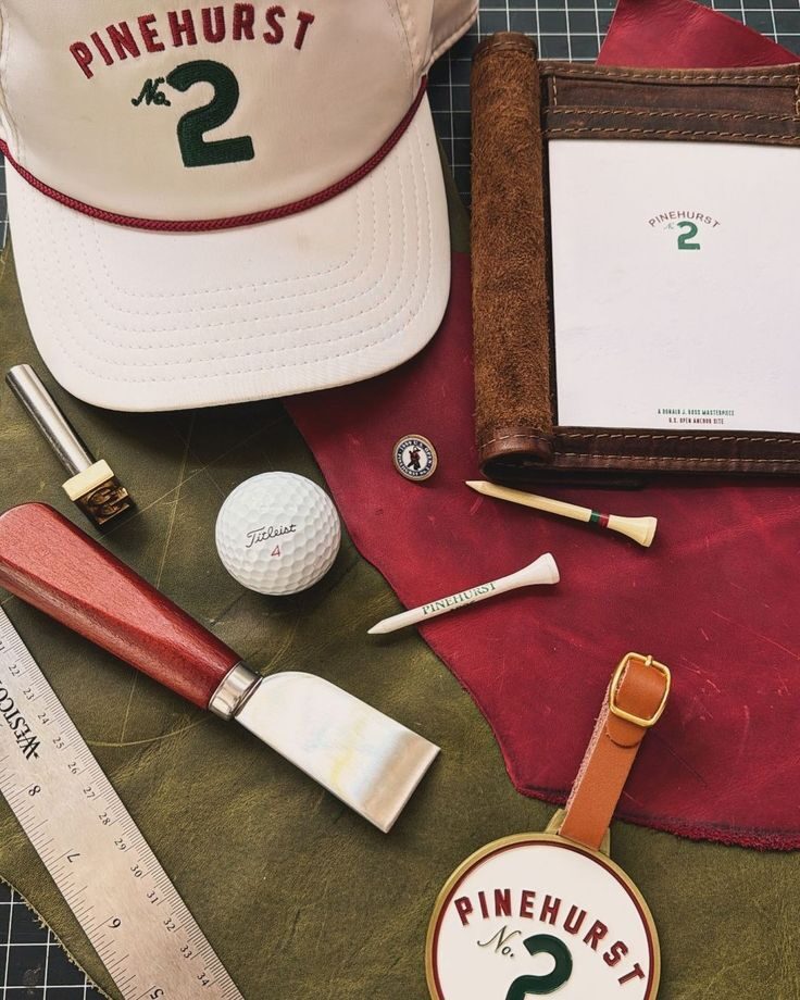Pinehurst flat lay with rope hat, Titleist ball, divot tool, tees, and leather bag tag