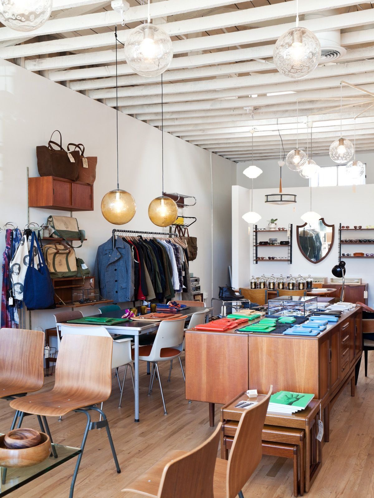 Bright shop interior with clothing rails, a centre table of folded knits and globe pendants