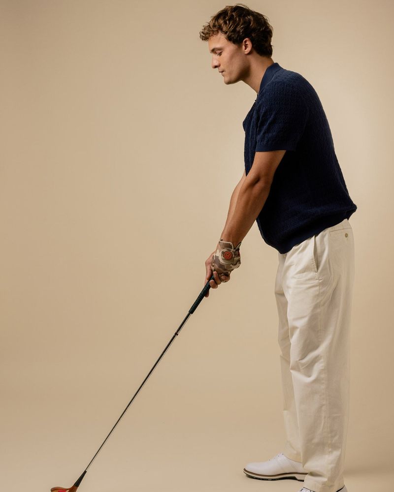 A golfer addressing a ball in the navy Lionel knitted polo