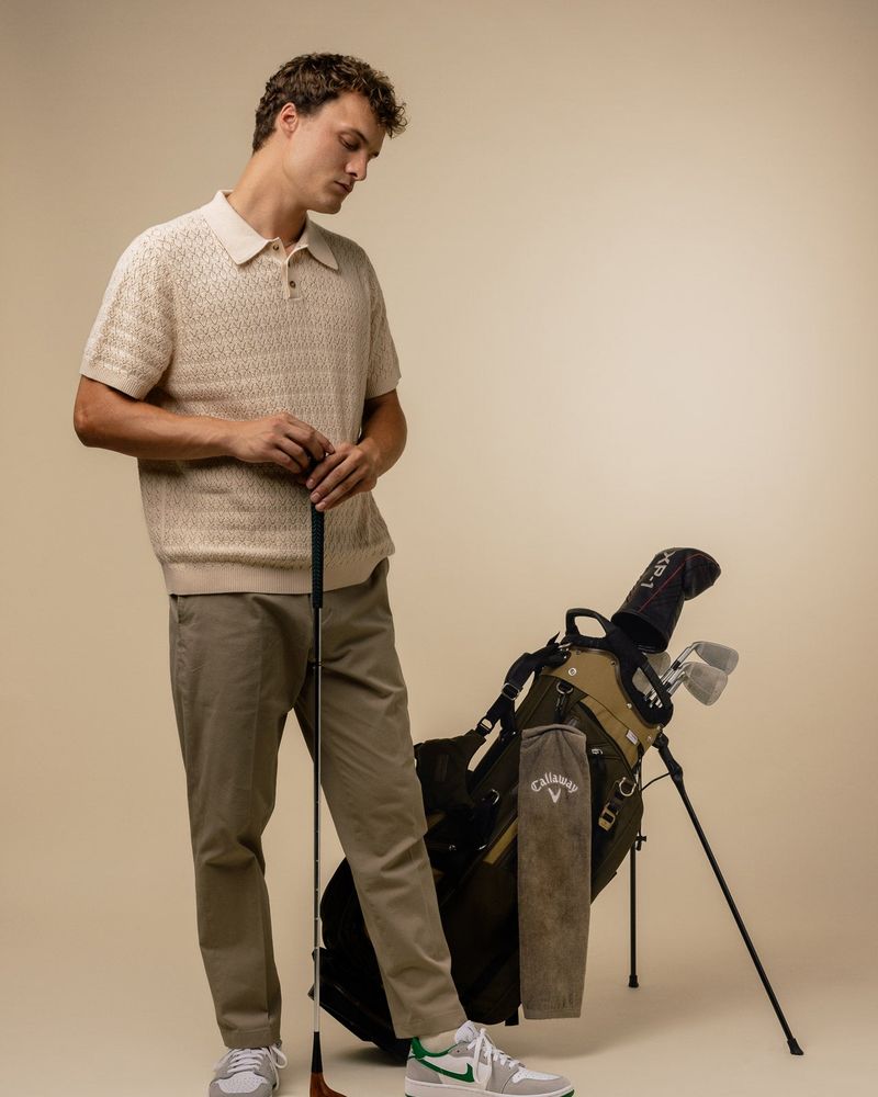 A model in a cream knitted polo beside a stand bag