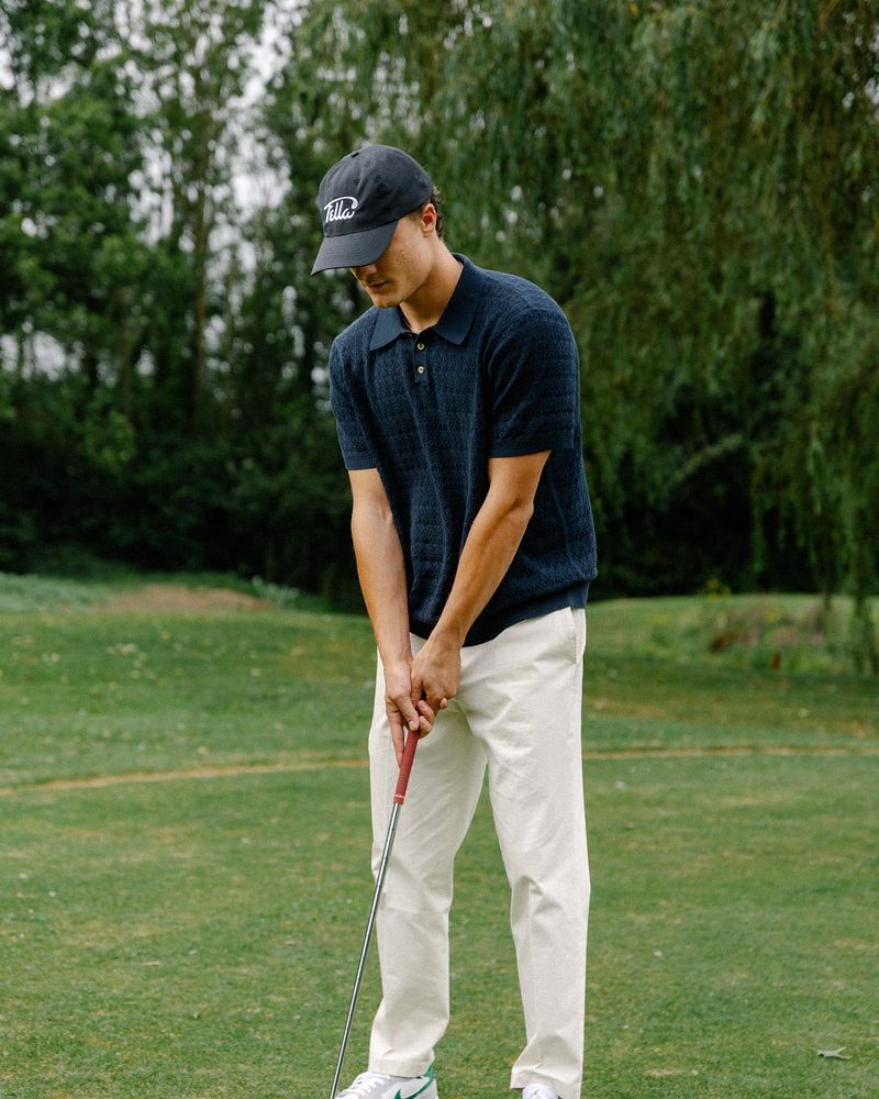 A golfer in a black Fella performance cap addressing a ball on a course