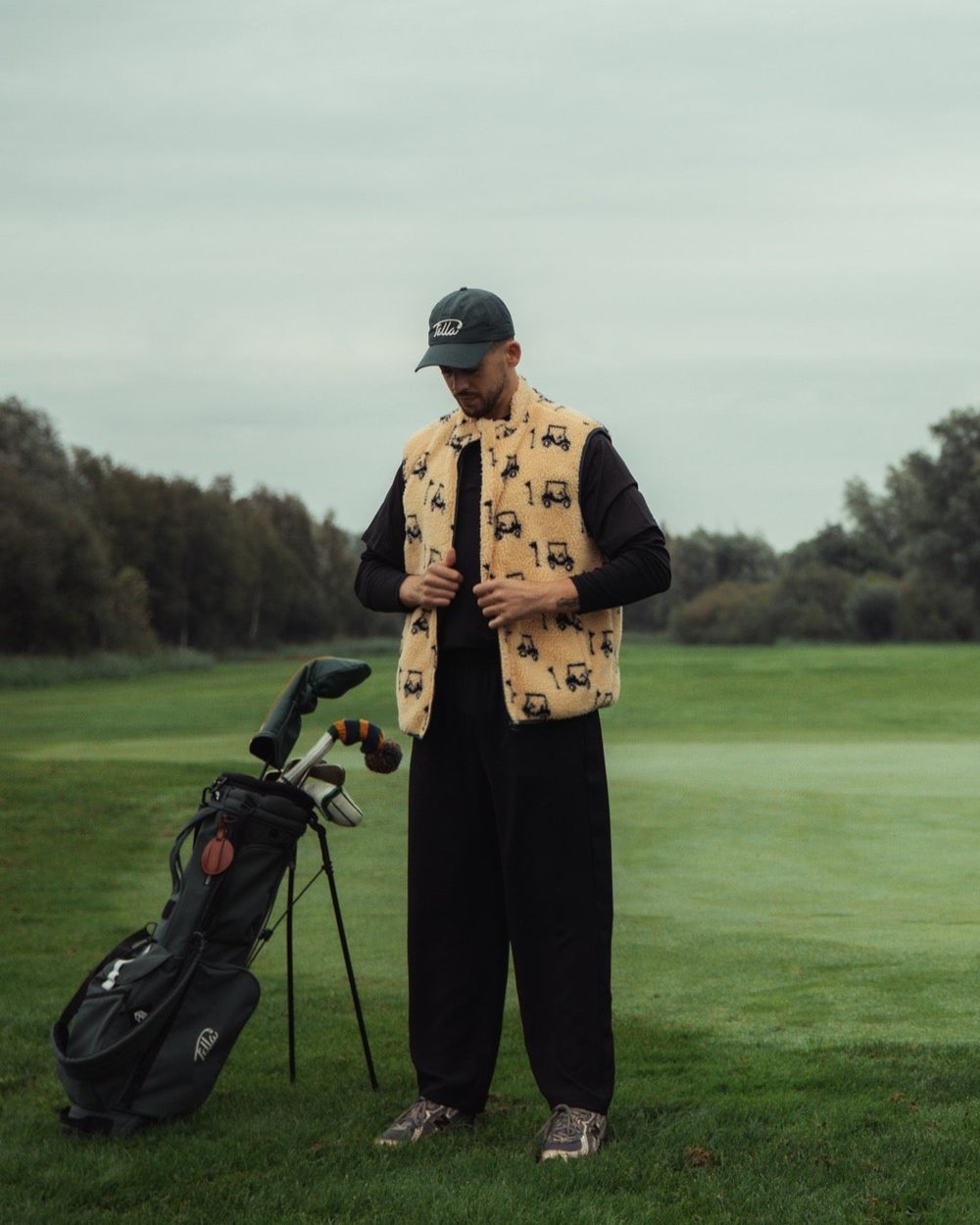 A golfer in a golf-cart print Fella bodywarmer beside his stand bag on the green