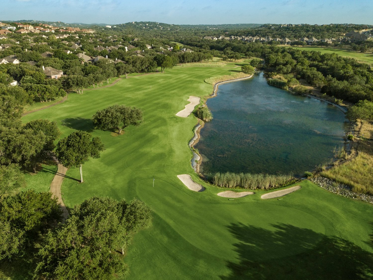 Aerial view of a fairway curving past a pond and oak woodland at Canyon Springs Golf Club, San Antonio