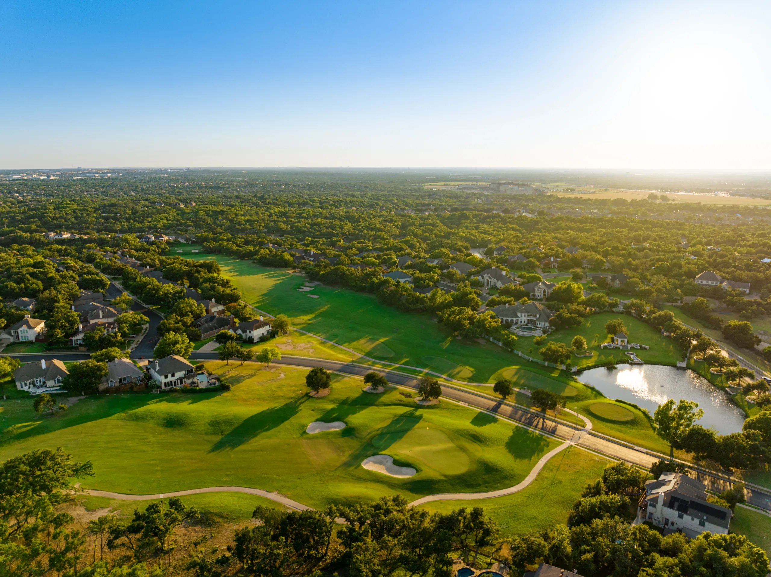 Aerial view of Forest Creek Golf Club in Round Rock, fairways and a pond among oak woodland at golden hour