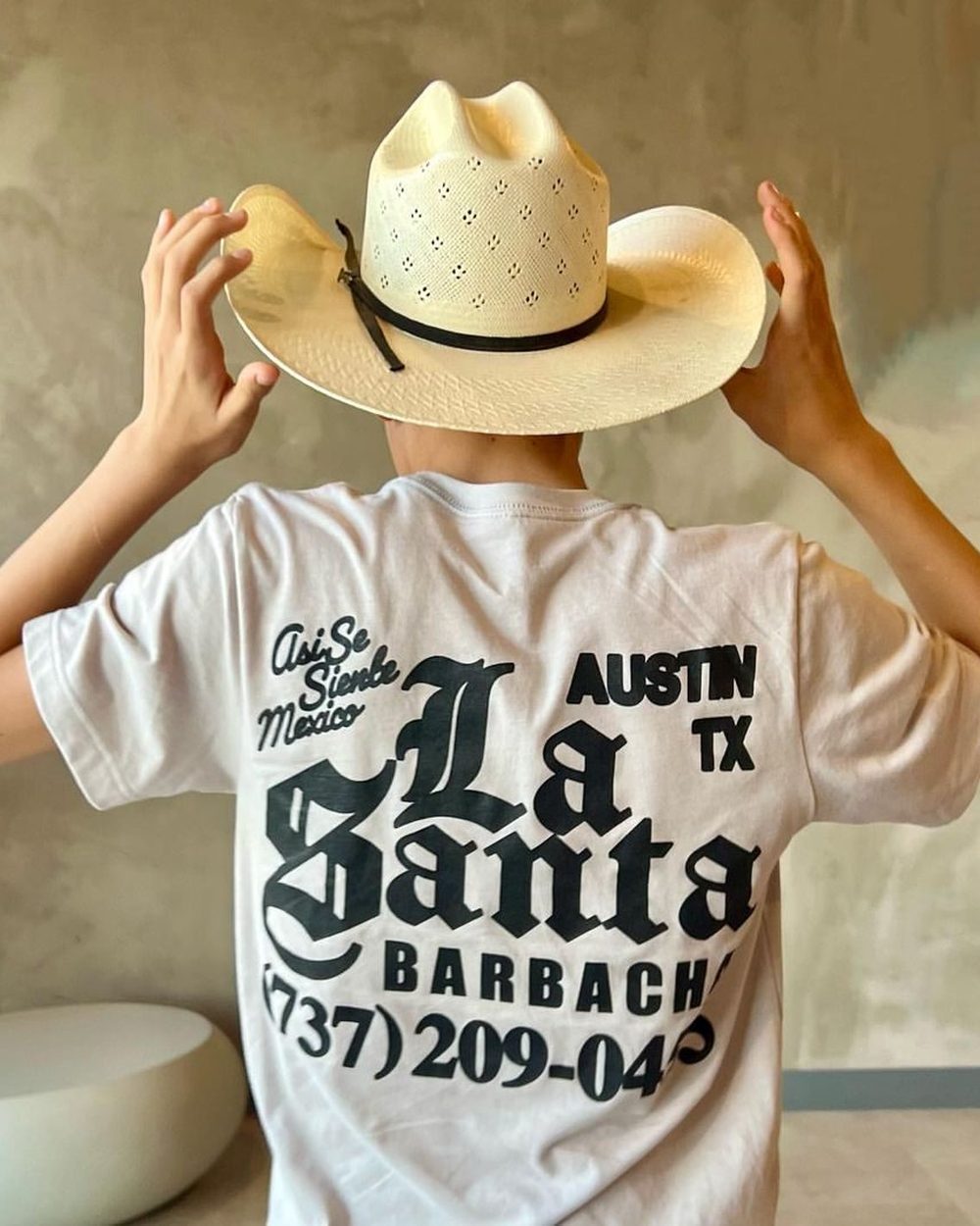 A person from behind in a cowboy hat and a La Santa Barbacha t-shirt