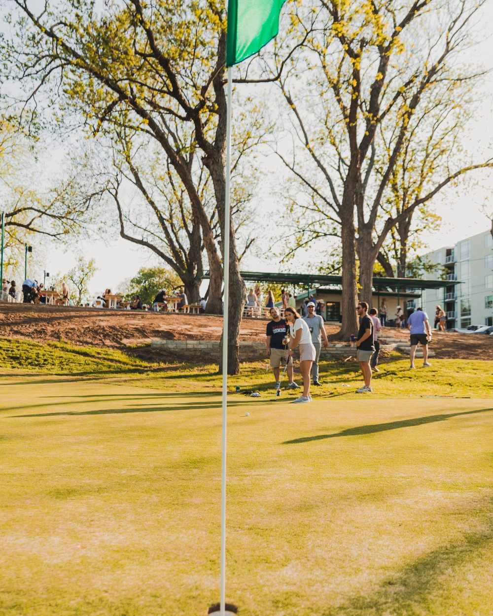 A green flag on a short hole at Butler Pitch & Putt with people playing behind