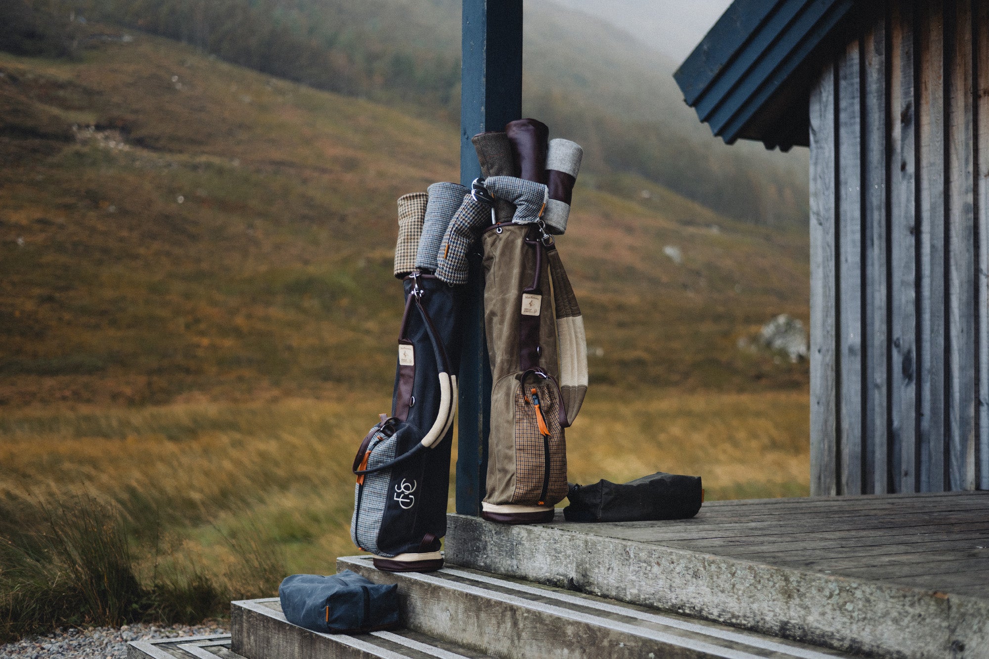 Two MacKenzie x Fyfe bags and shoe bags outside a Highland hut