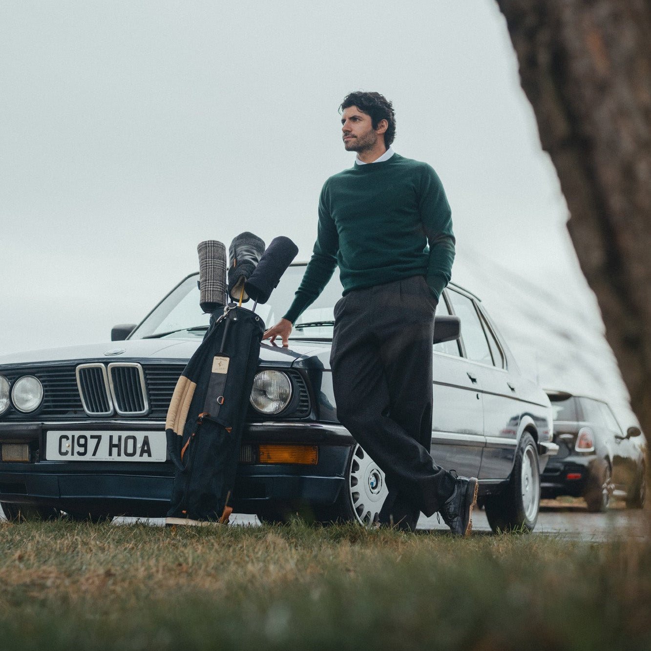 A man in a green crew neck leaning on the car with his bags