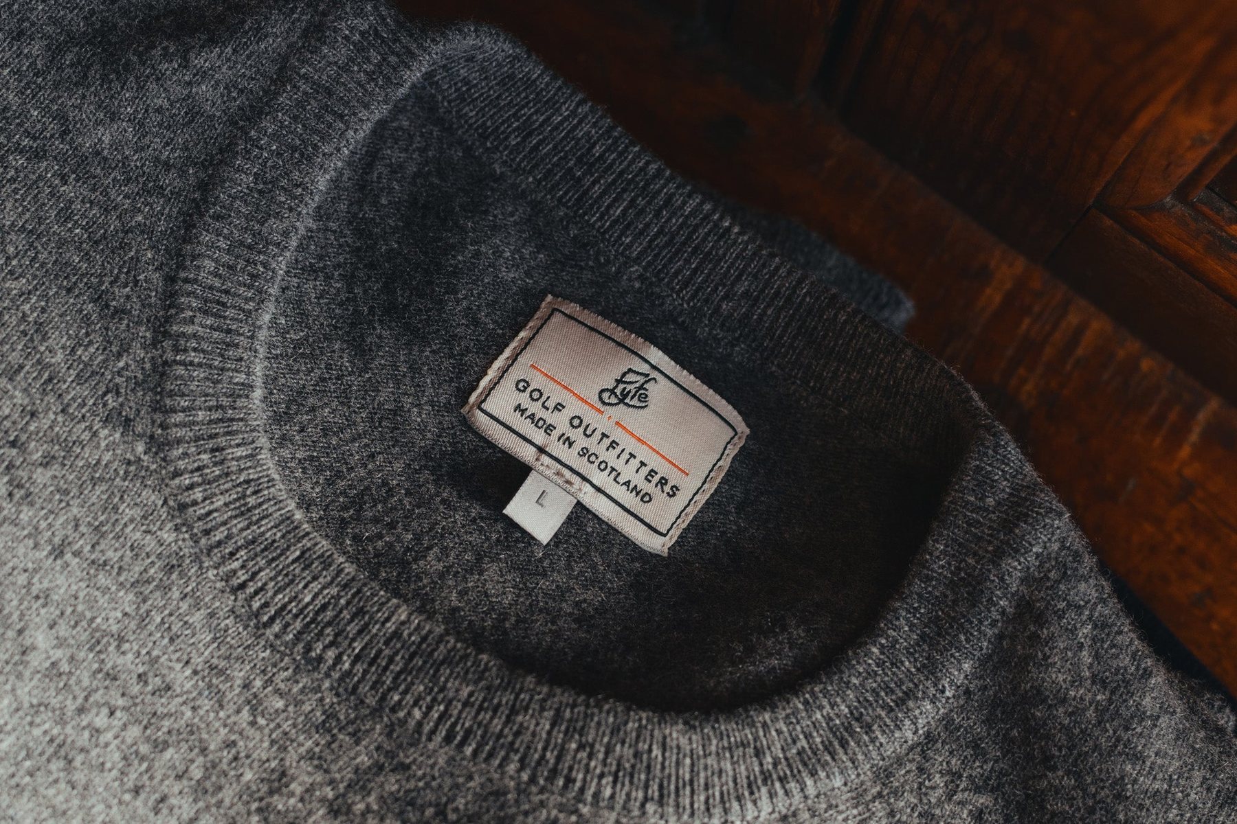 Close-up of a grey lambswool crew neck and its Fyfe label on a wooden bench