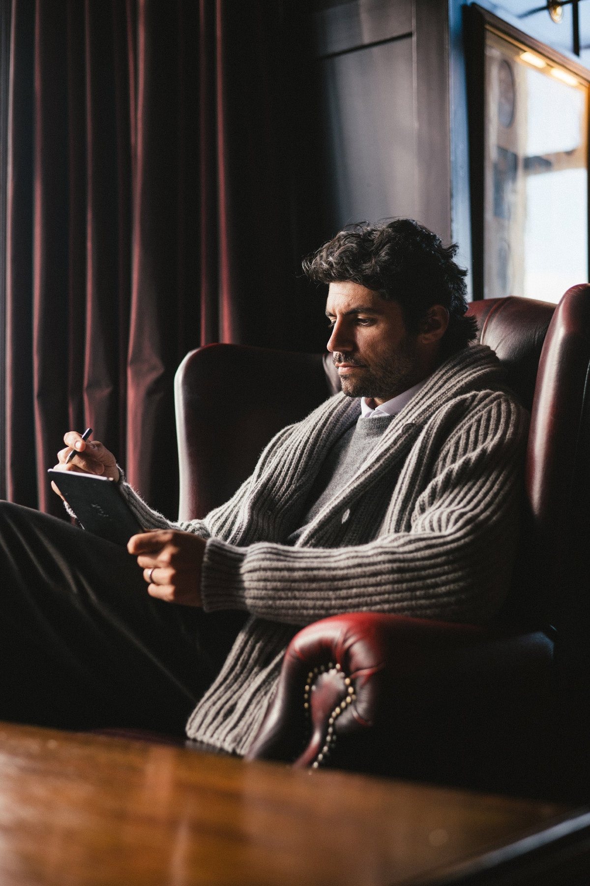 A man reading in a leather chair by a window
