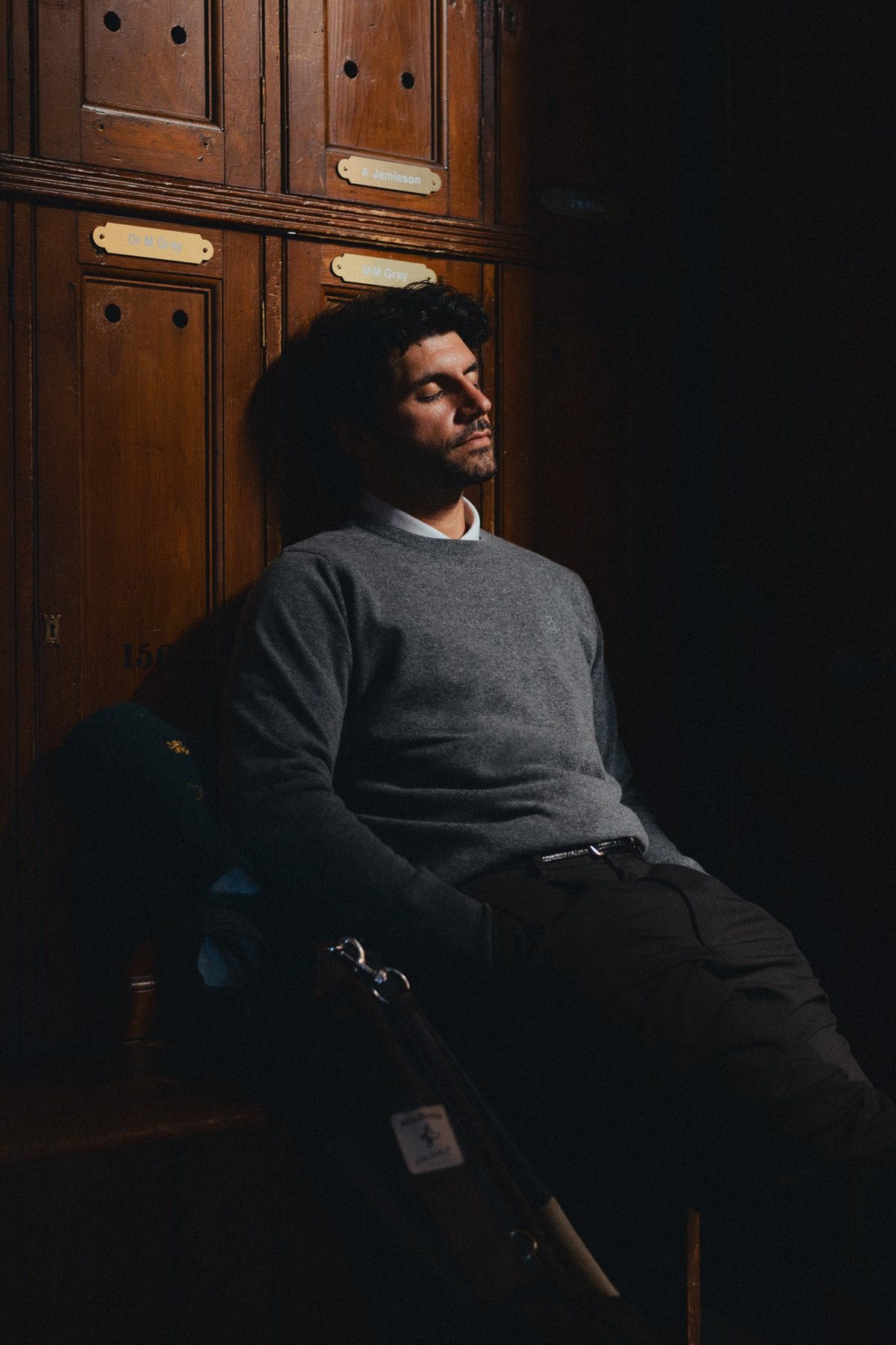 A man in a grey crew neck leaning back in a dark locker room