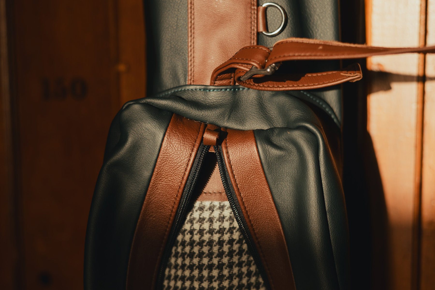 Close-up of a golf bag&rsquo;s leather straps and houndstooth tweed in warm low light