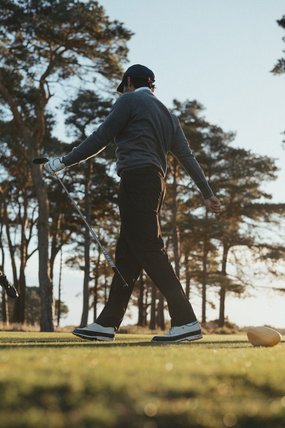 A golfer walking across the course in a grey knit