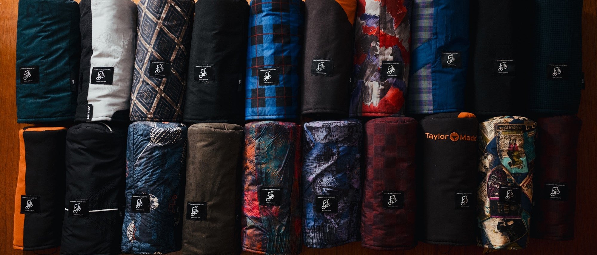 Fyfe Golf Second Round headcovers lined up in two rows on a wooden table, cut from vintage golf jackets