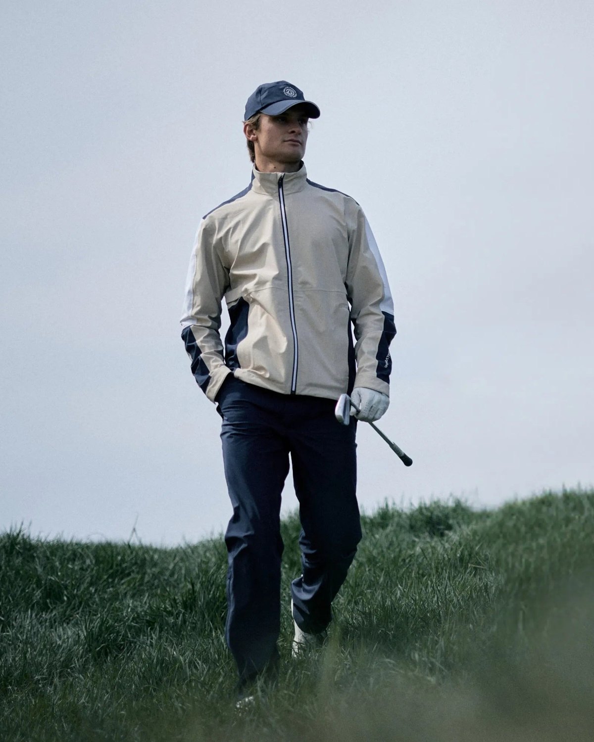 A golfer walking off a links fairway in a pale grey Galvin Green jacket