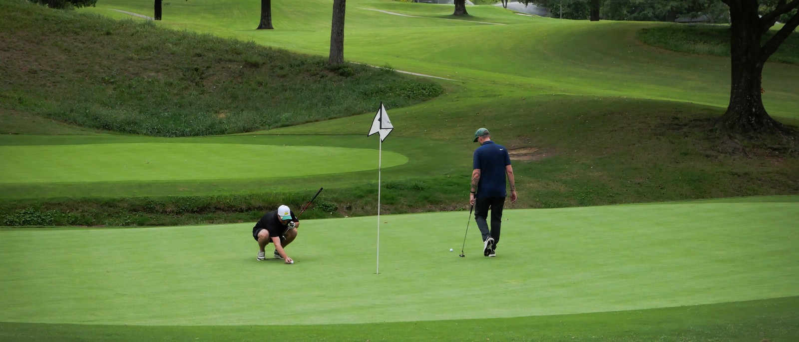A golfer walking up to a green framed by mature trees, from Gamut Golf's own course photography