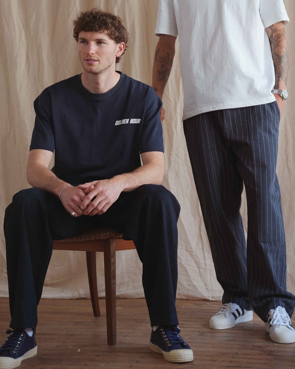 Two men in Golden Hour tees, one seated on a wooden chair