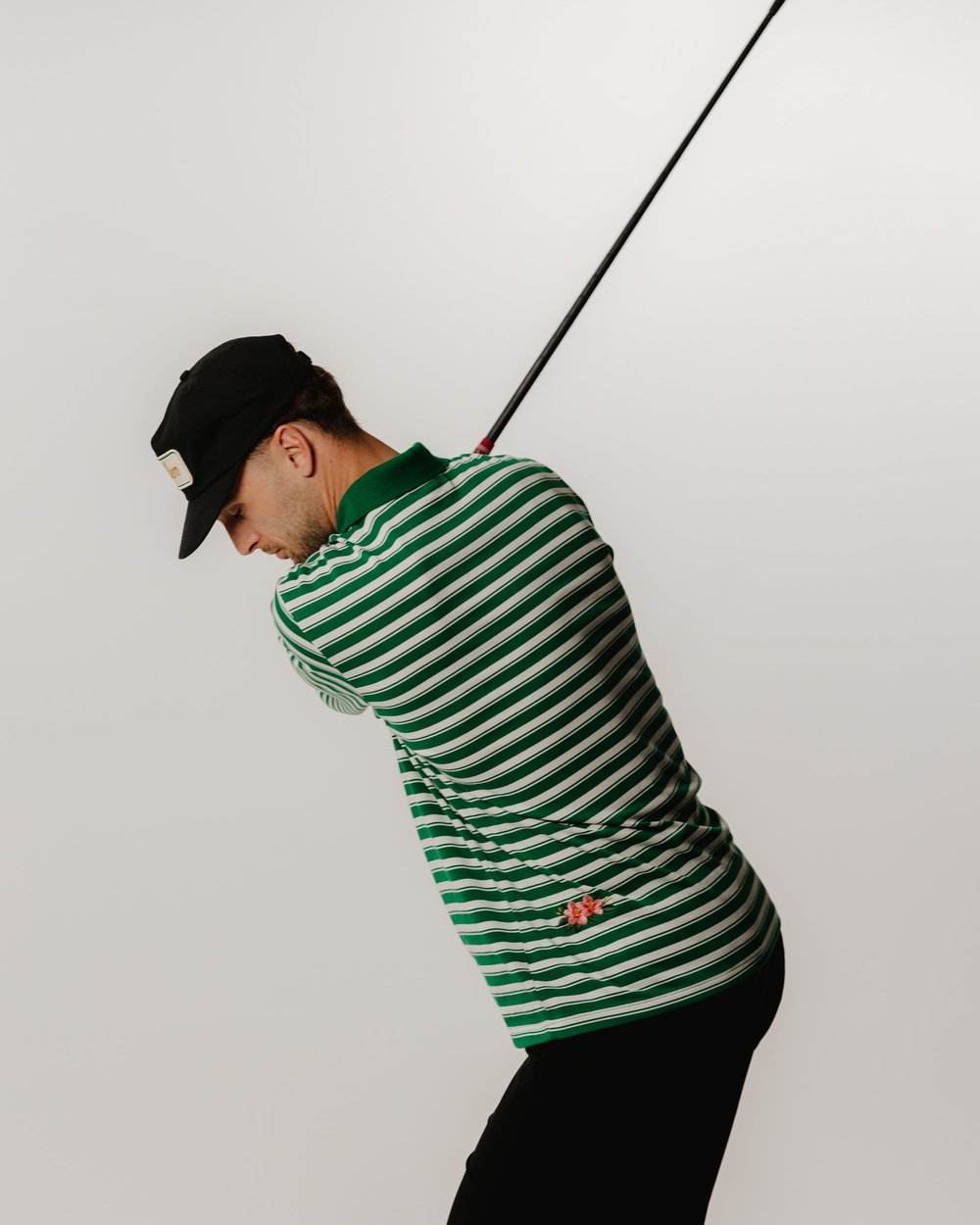 A golfer swinging in the green striped polo