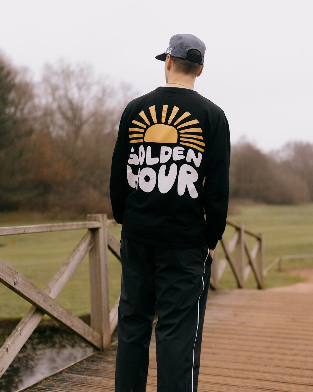 A golfer from behind in a black long-sleeve with a sunset Golden Hour print