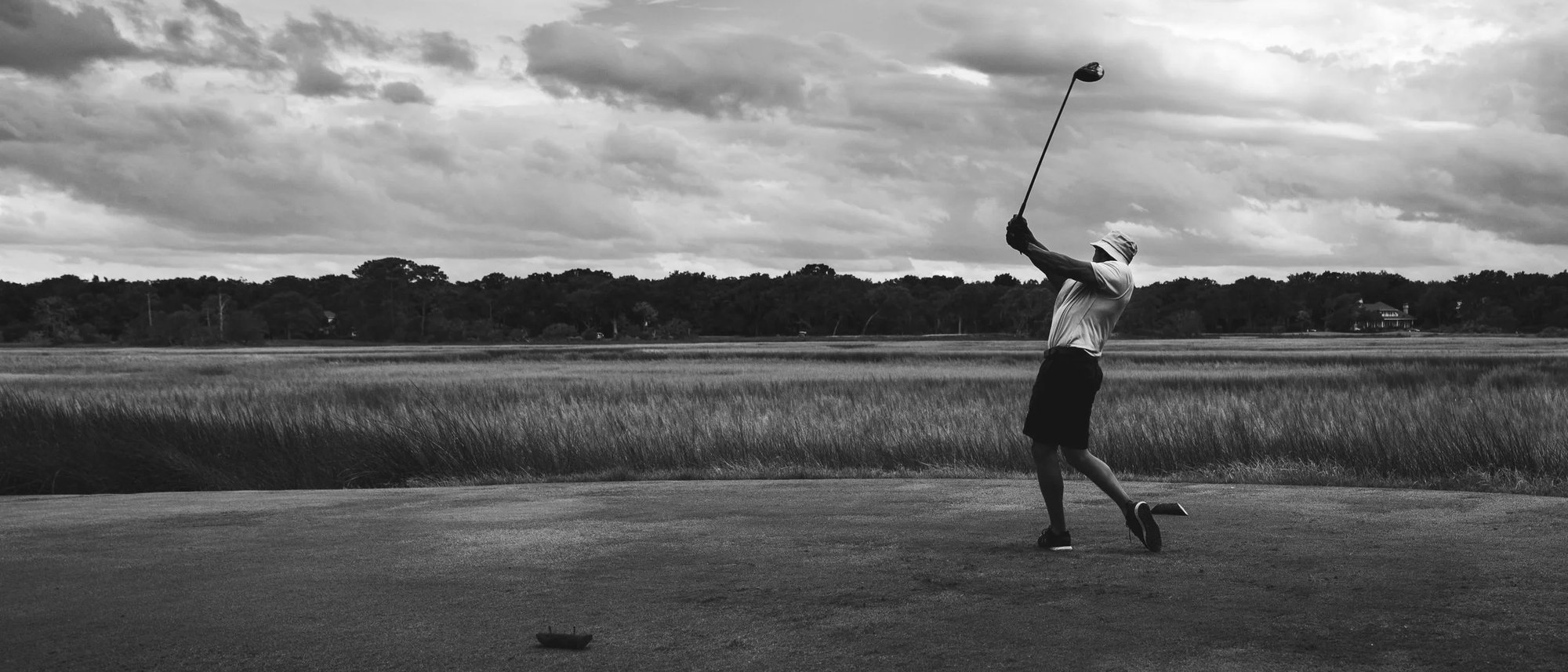 A golfer mid-swing on an open course under a big sky, in black and white, from Golden Soul Golf