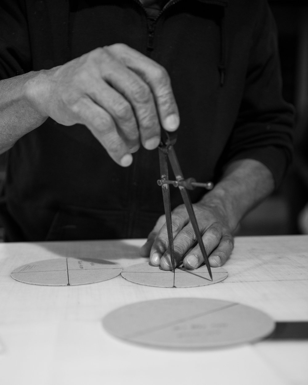 Hands drawing a circle pattern with a compass on paper