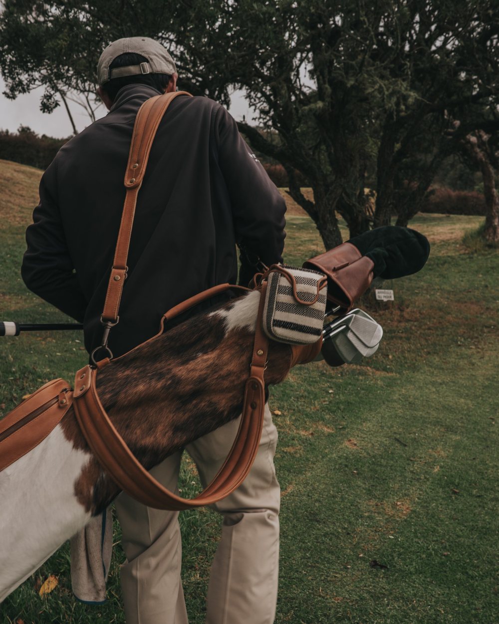 A golfer carrying a cowhide and leather carry bag through trees