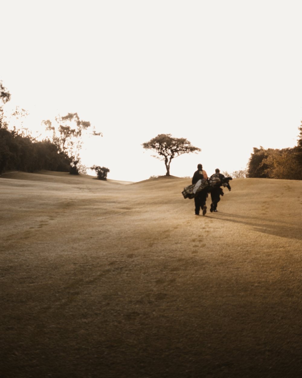 Two golfers walking down a sandy fairway carrying bags
